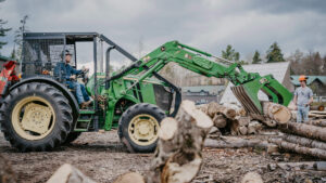 Student operating an earth mover to transport logs