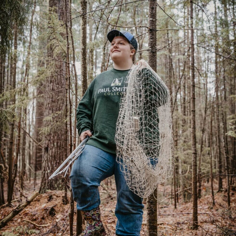 Student holding a net walking through the woods