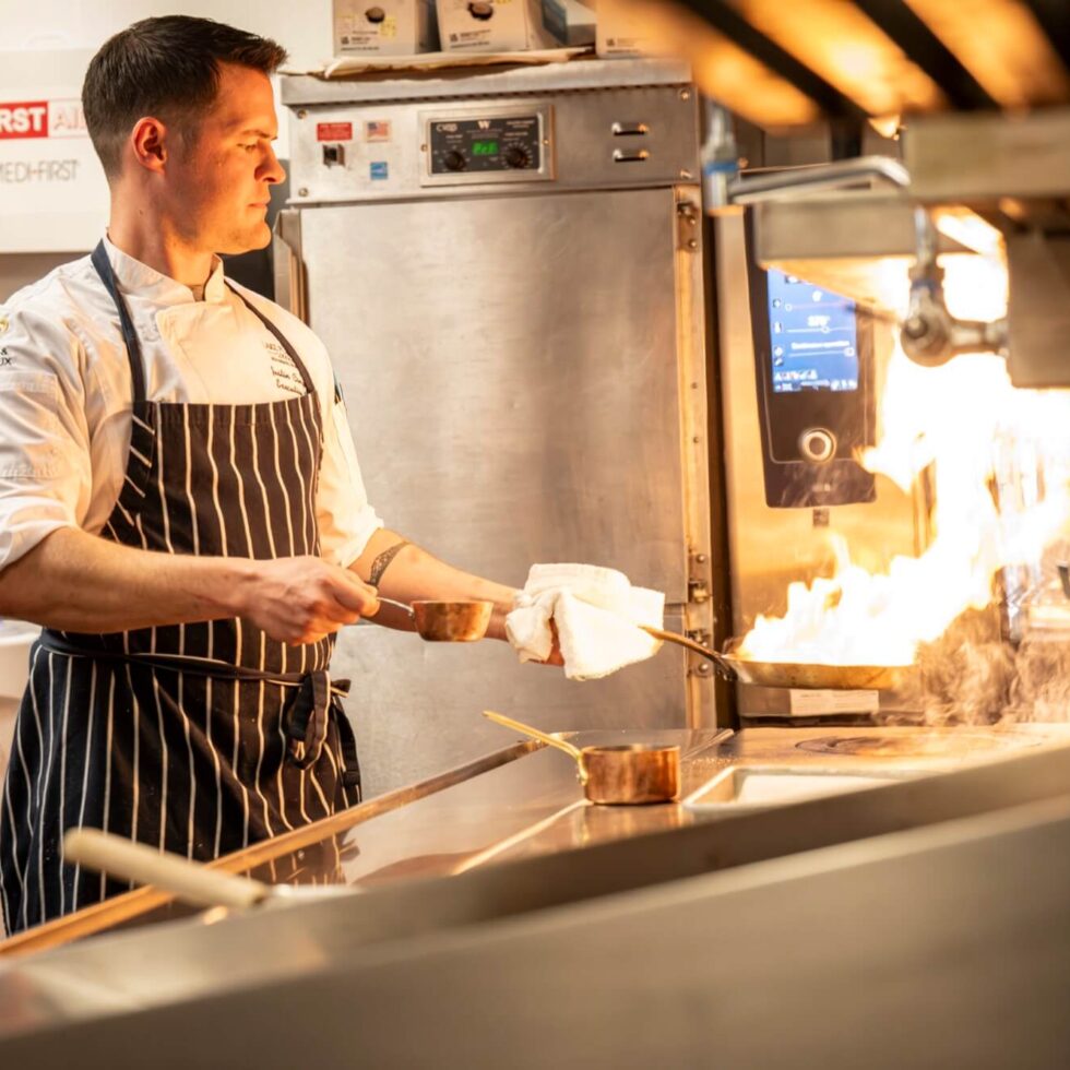 A chef holding a pan with flames coming off of it