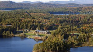 Aerial view of the Paul Smith's College campus with a lake in the foreground and mountains in the distance