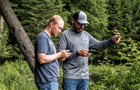 Pair of Paul Smith's students looking at their phones while on a walk in the woods